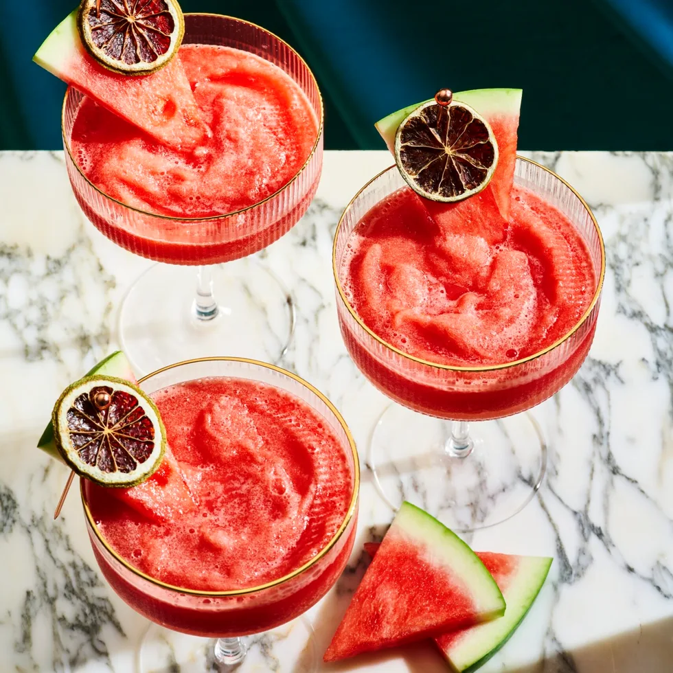 3 watermelon daiquiri's on a marble board, with a wedge of watermelon and a dried lime ontop of the cocktail as a garnish
