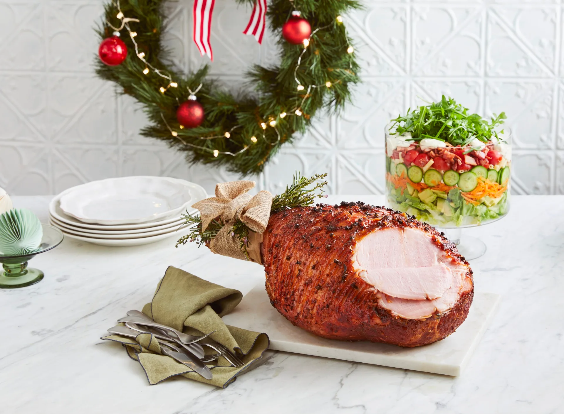 honey mustard ham with christmas tie on the end with layered pasta salad in trifle stand on the side with wreath in the background
