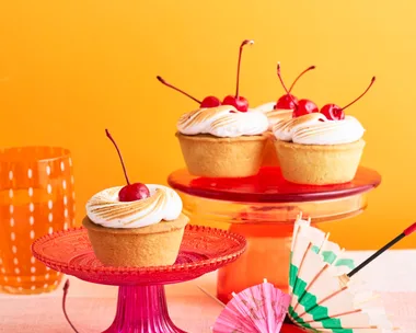 amaretto sour bakewell tart topped with a cherry, sitting on a pink cake stand in front of an orange background