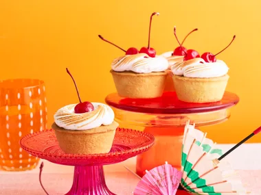 amaretto sour bakewell tart topped with a cherry, sitting on a pink cake stand in front of an orange background