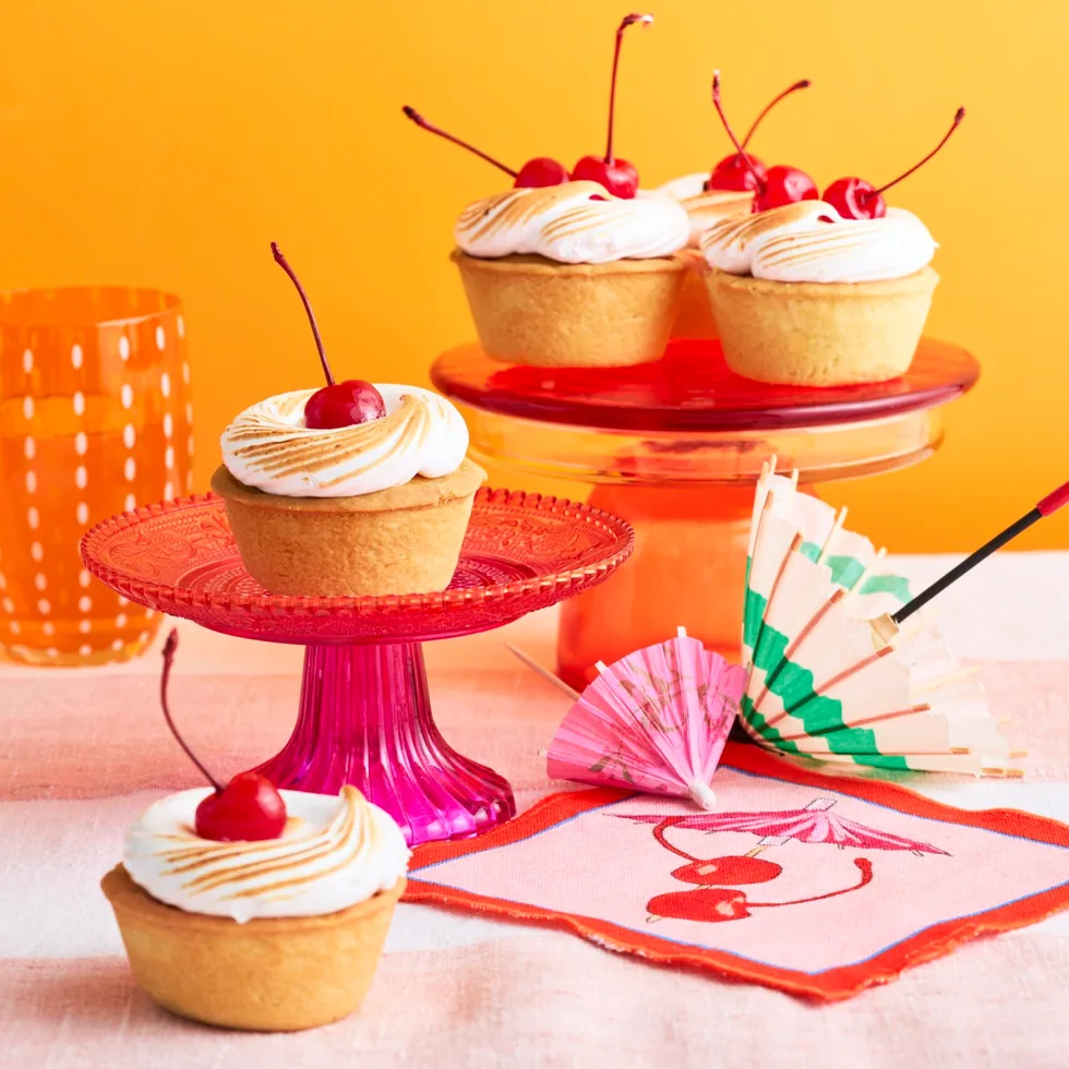 amaretto sour bakewell tart topped with a cherry, sitting on a pink cake stand in front of an orange background