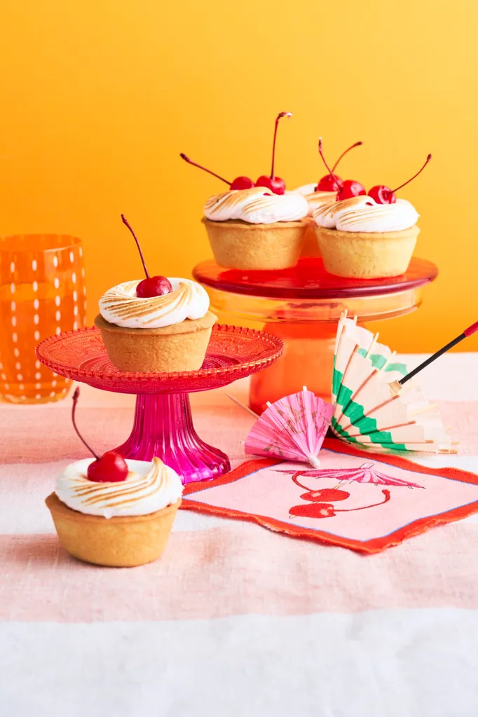 amaretto sour bakewell tart topped with a cherry, sitting on a pink cake stand in front of an orange background