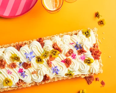 A rectangular cheesecake with a swirled pattern cream top with scattered edible flowers to decorate. On a yellow background