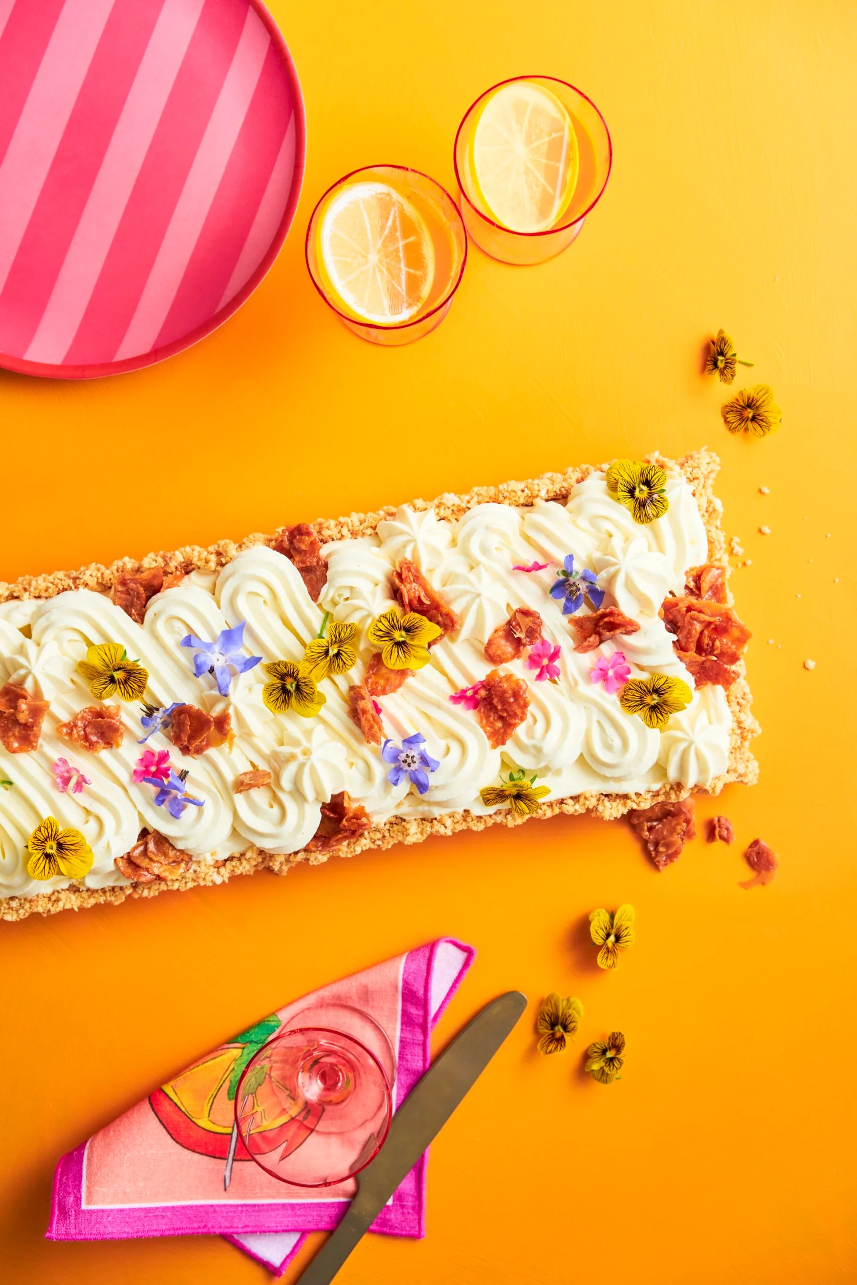A rectangular cheesecake with a swirled pattern cream top with scattered edible flowers to decorate. On a yellow background