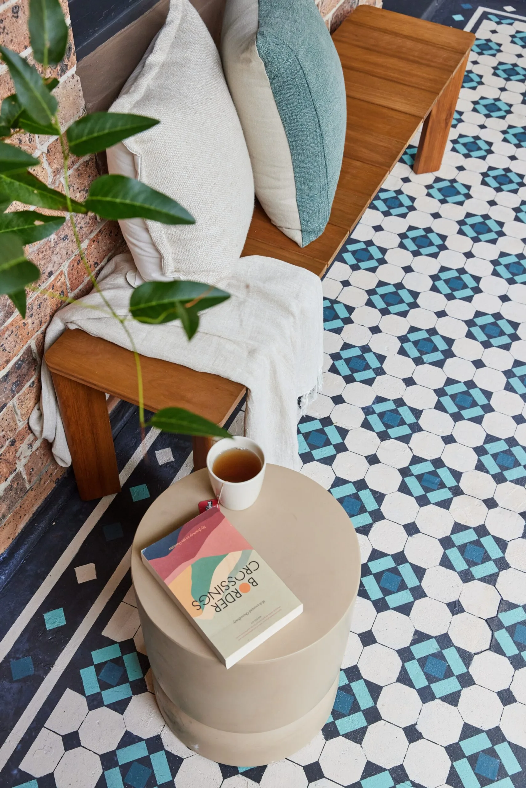 wooden bench with cushions and blanket on it and front concrete porch floor stencilled with blue and aqua Federation style design with paint.