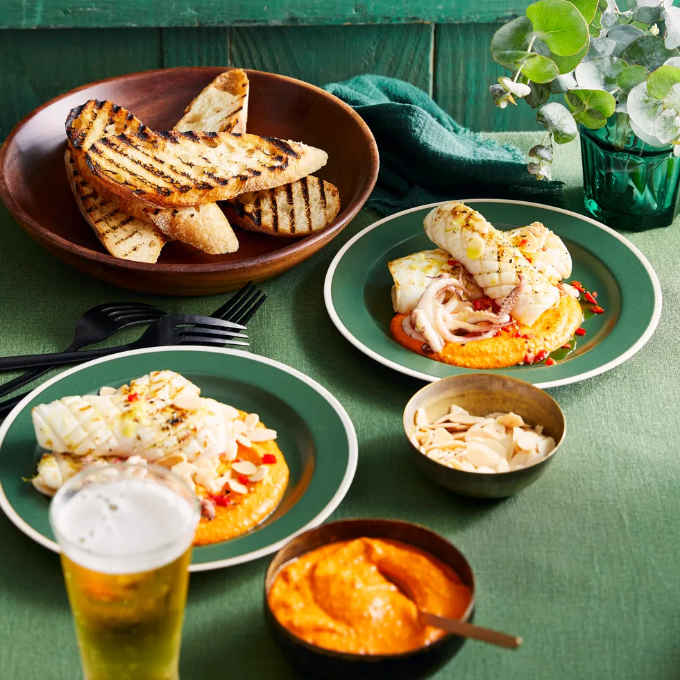 grilled squid with romesco orange sauce on the bottom, chargrilled bread slices in background