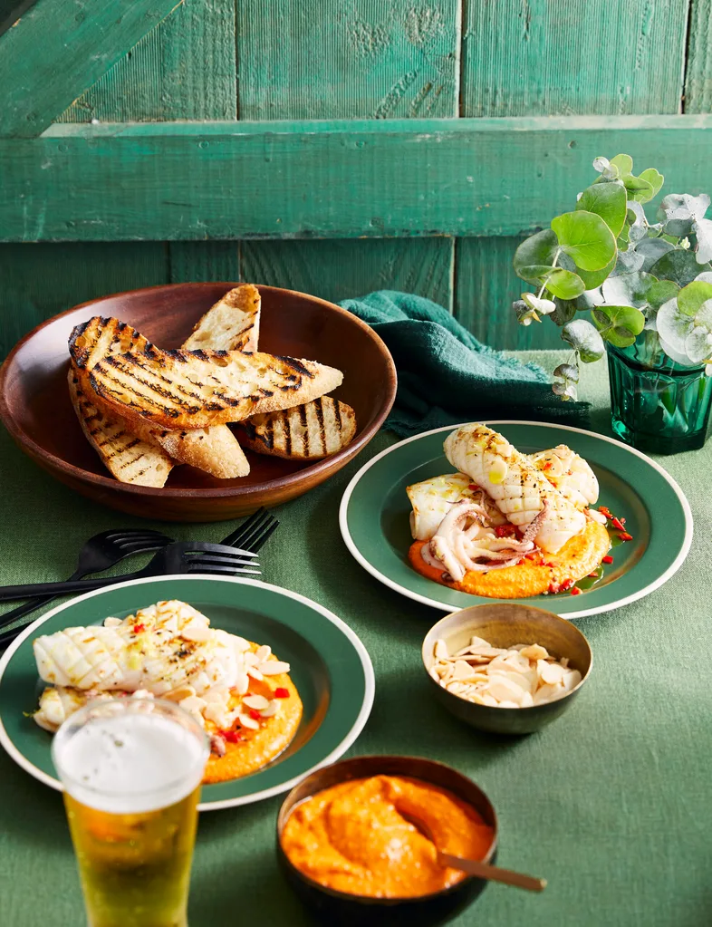 grilled squid with romesco orange sauce on the bottom, chargrilled bread slices in background
