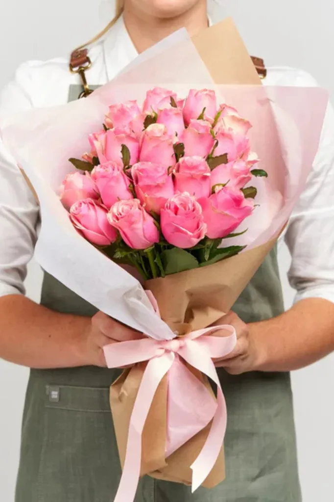 bunch of pink roses being held by florist in grey apron