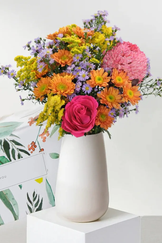 colourful orange yellow and pink flowers in white vase for mother's day