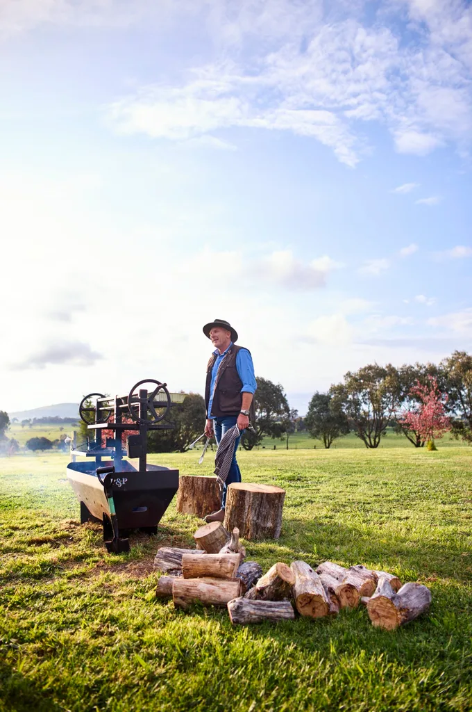 farm owner standing in grass field with fire wood and bbq