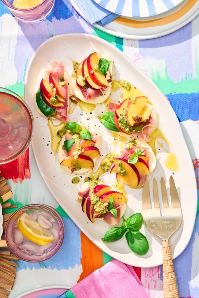 a white plate with mozzarella slices, topped with prosciutto and yellow nectarine