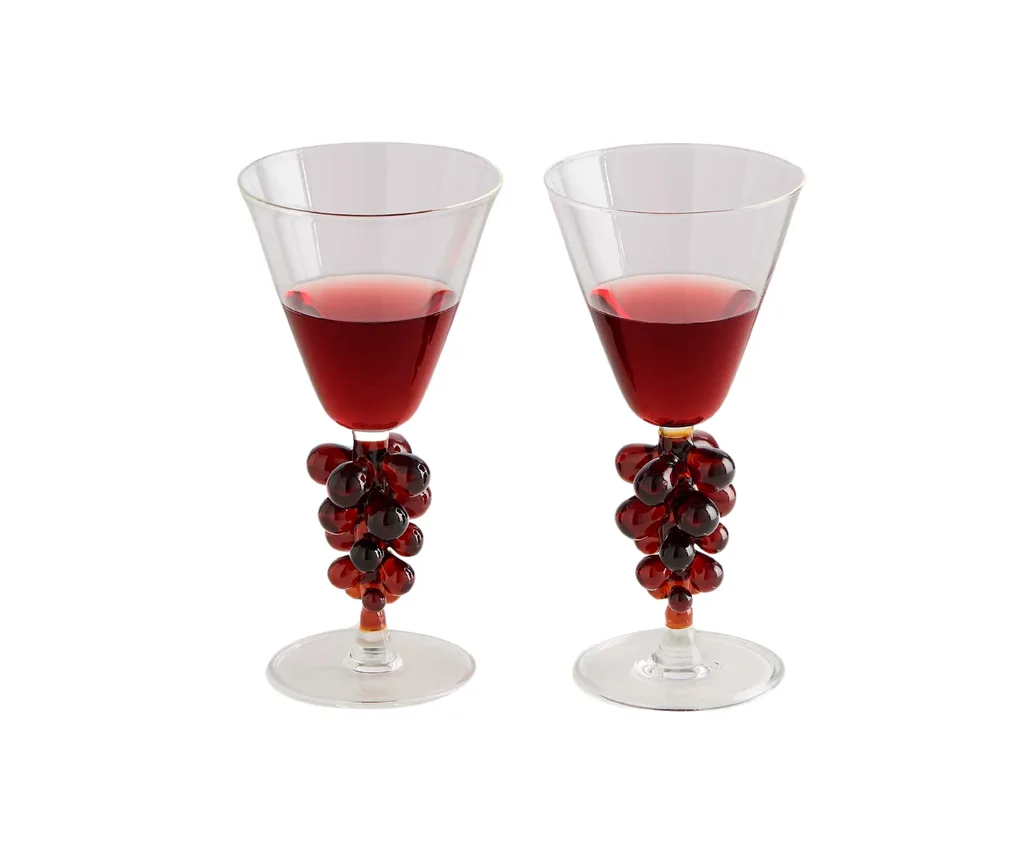 wine glasses half full with red wine and a glass grape decoration on the bottom of them