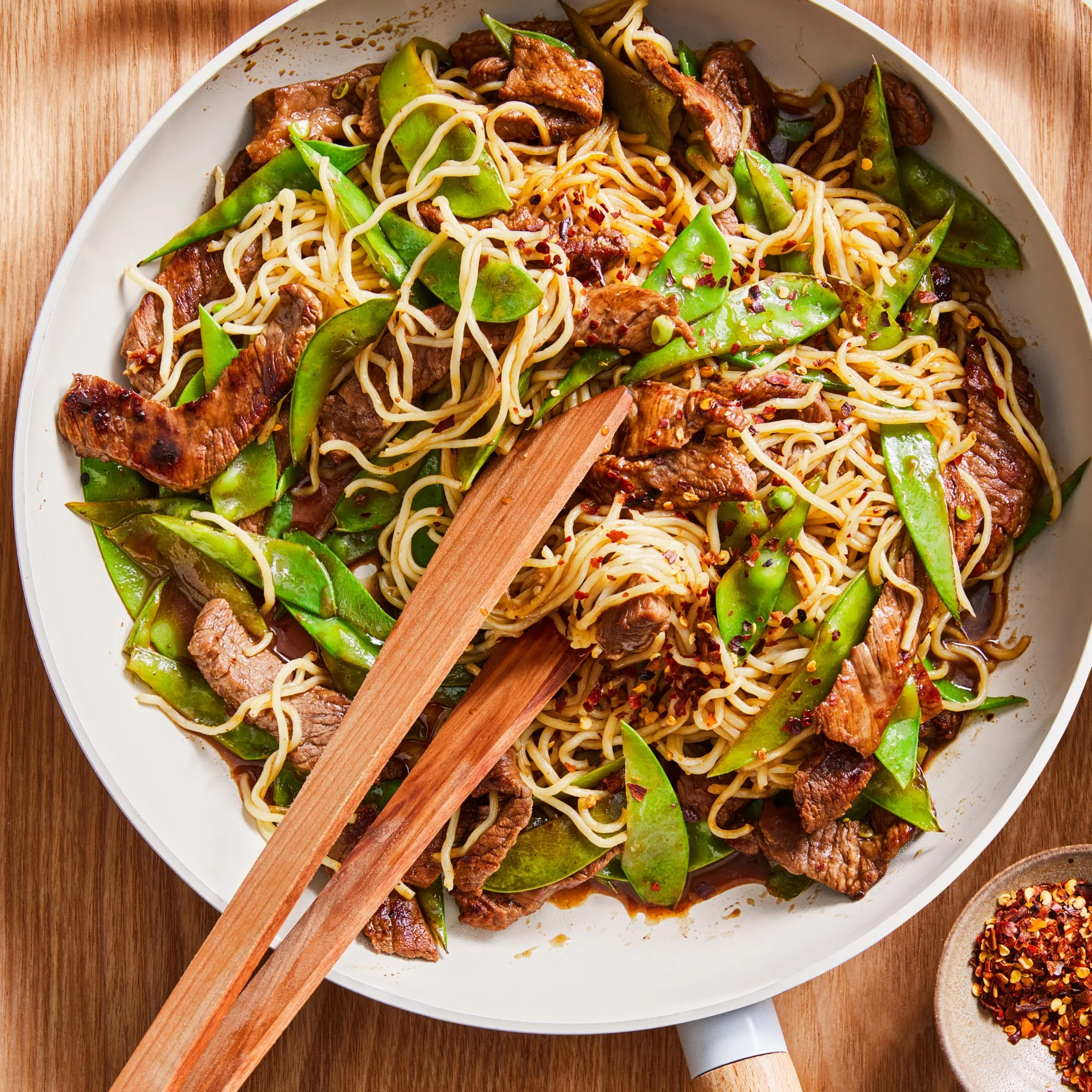 steak stir fry with snow peas and noodles and tongs in bowl
