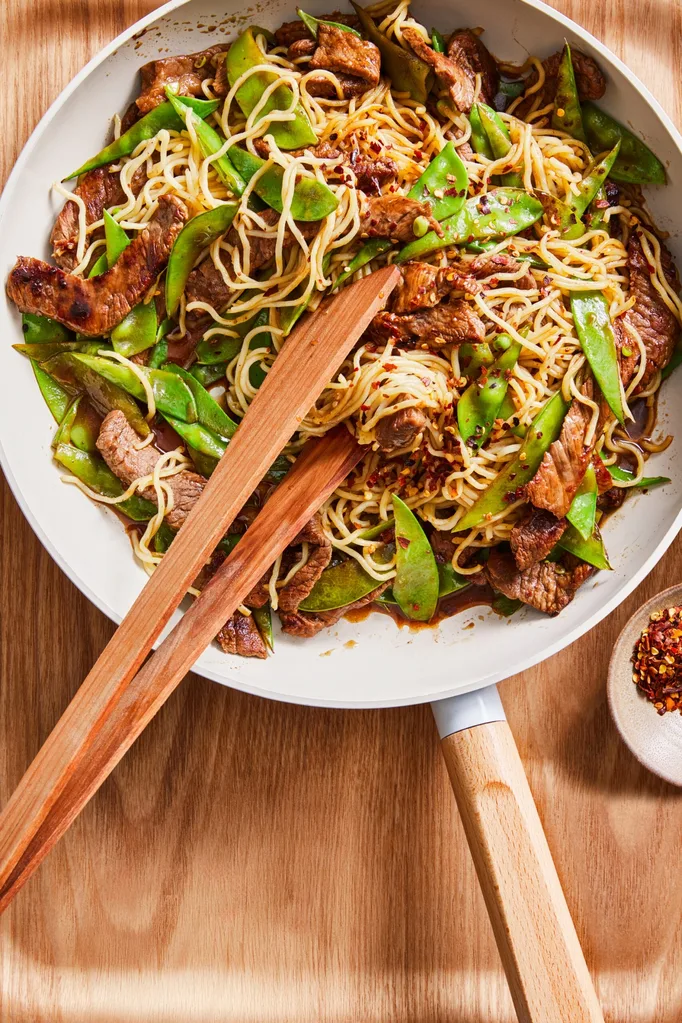 steak stir fry with noodles and tongs in it