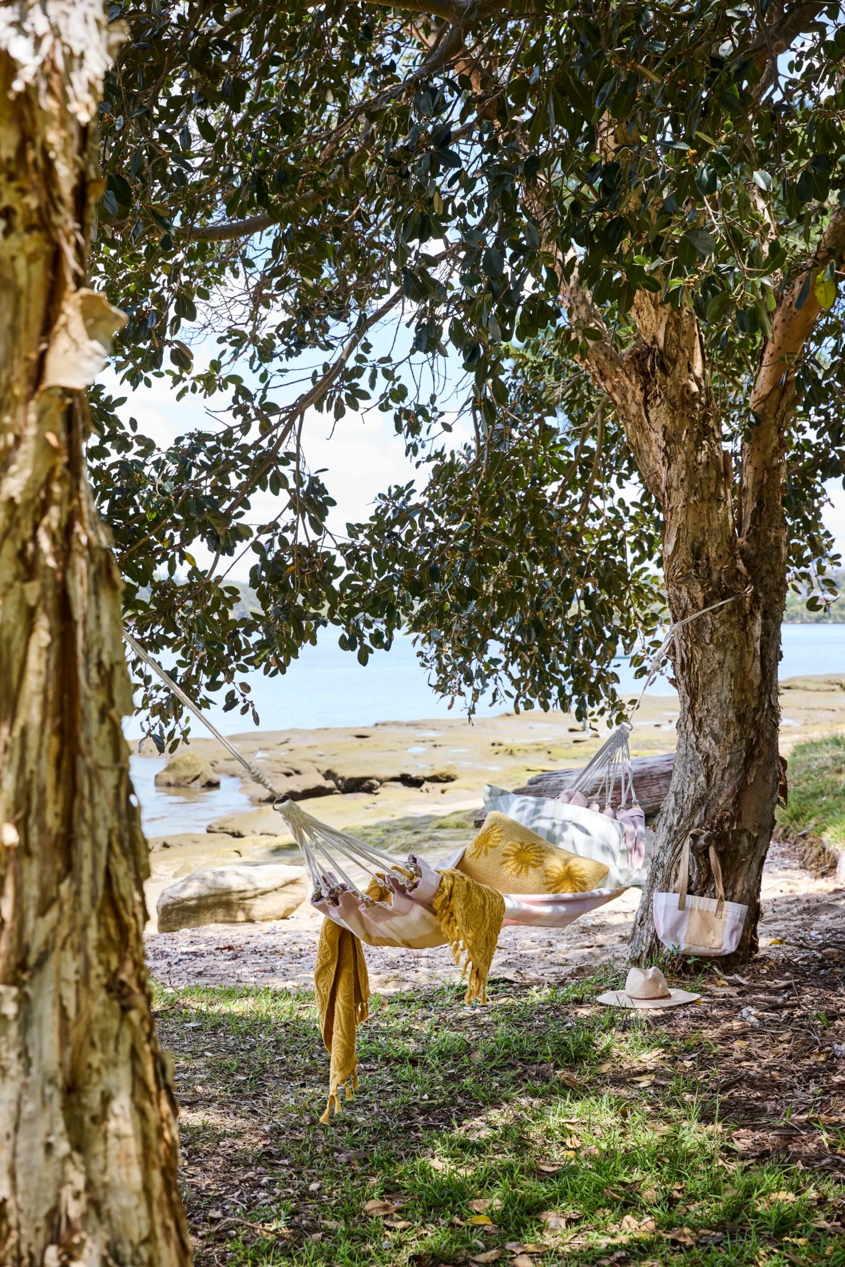 a pink hammock filled with cushions hanging between 2 trees on waterfront beach location