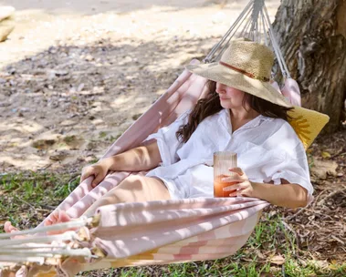 a woman wearing hat and white shirt lounging in a pink hammock