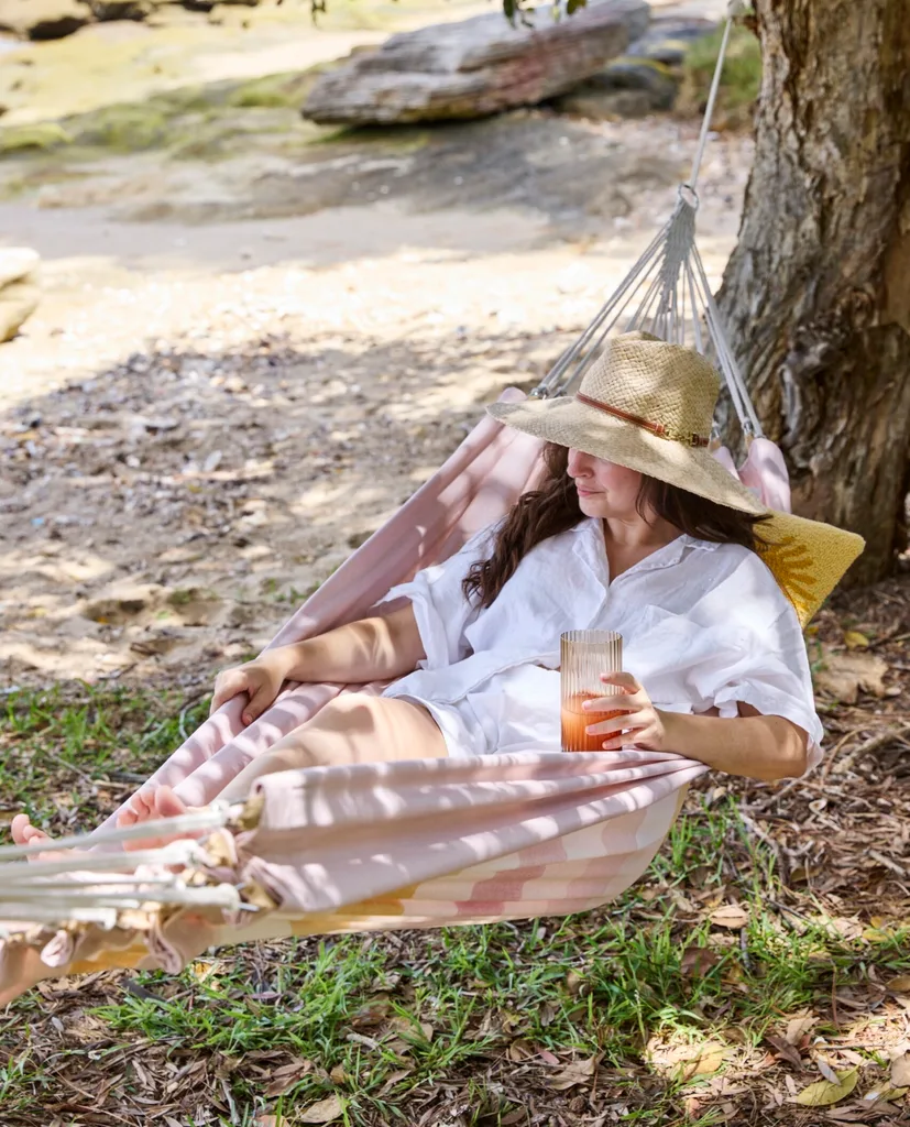 a woman wearing hat and white shirt lounging in a pink hammock