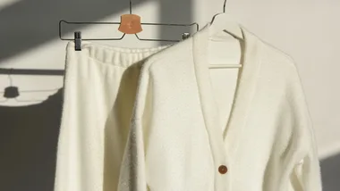 a cream wool set featuring a cream cardigan and cream pants hanging on a rack