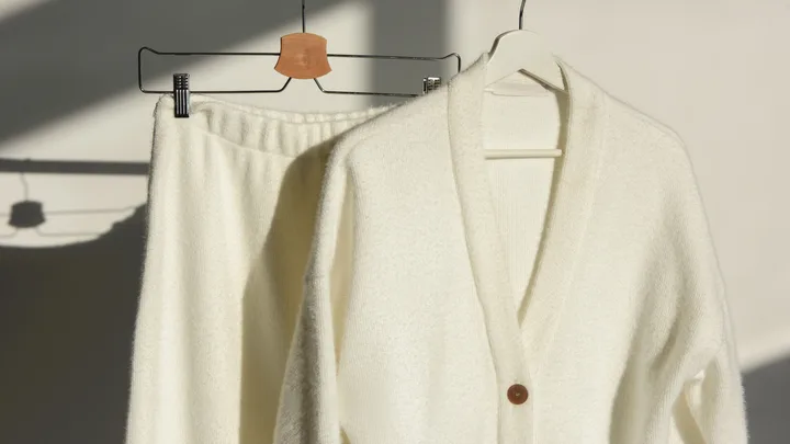 a cream wool set featuring a cream cardigan and cream pants hanging on a rack