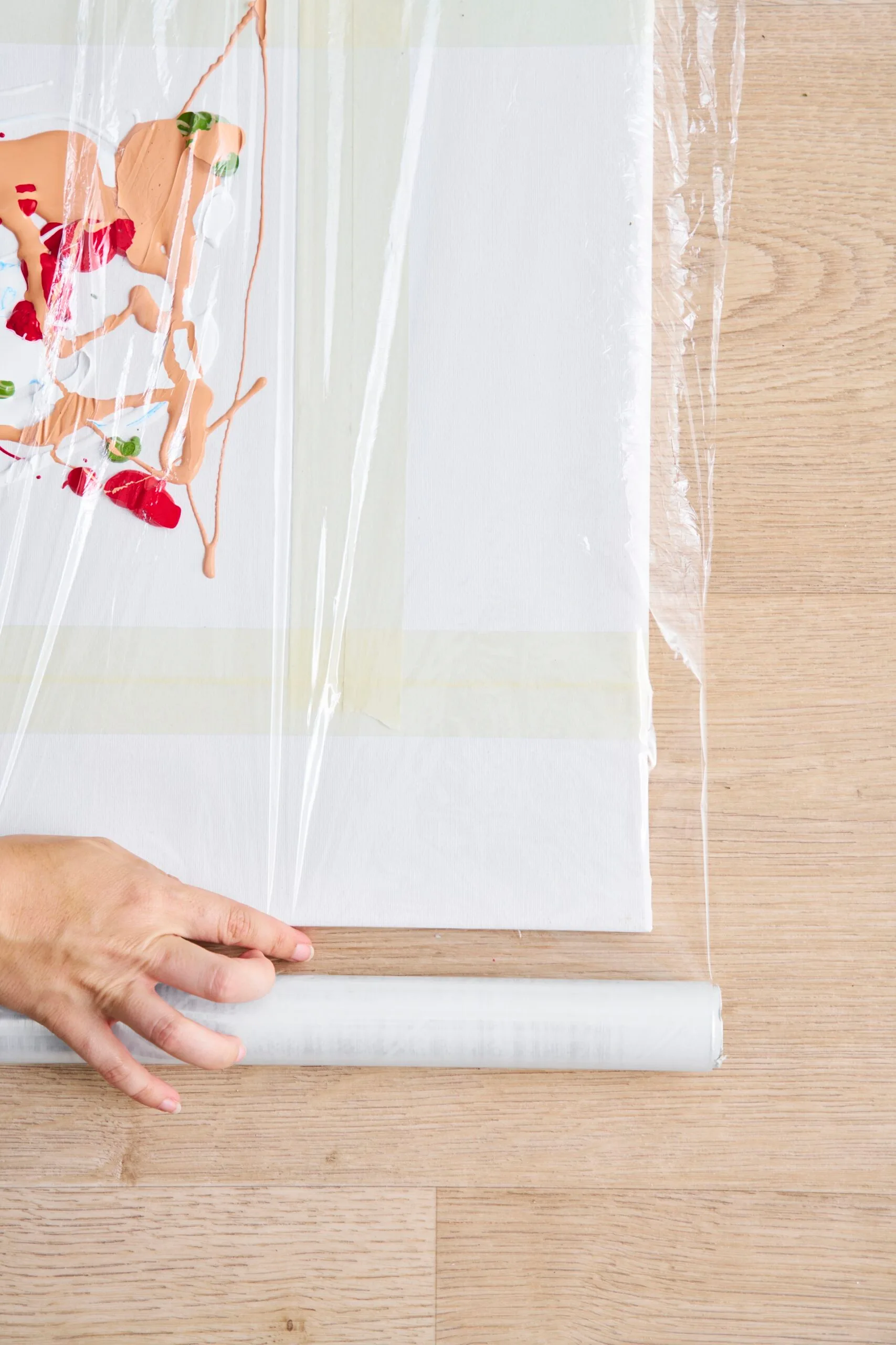canvas with peach, red and green paint oniit and being covered with cellophane wrap.