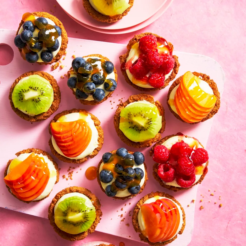 individual fruit tarts shot from birds eye view with blueberries, kiwi, peach and raspberries on them