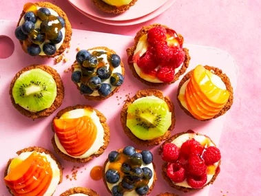 individual fruit tarts shot from birds eye view with blueberries, kiwi, peach and raspberries on them