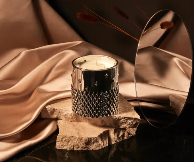 Styled shot of House of Scandal 'Trophy Wife' candle on a rock platform in front of a mirror