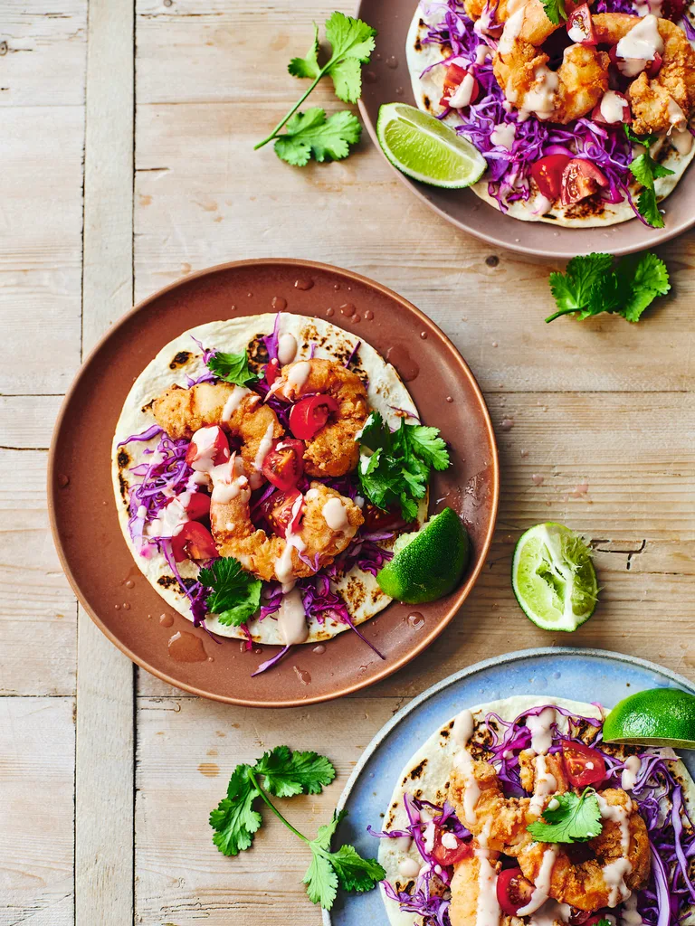 three plates of bang bang prawn tacos with cabbage slaw and lime and coriander on top
