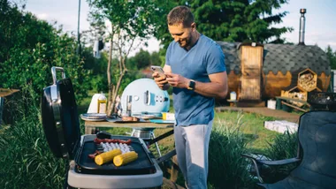 A smiling man using a smart phone at a backyard bbq.