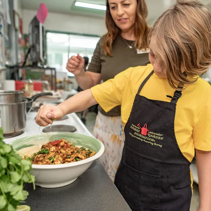 child in yellow tshirt making sundried tomato pasta with apron on