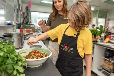 child in yellow tshirt making sundried tomato pasta with apron on