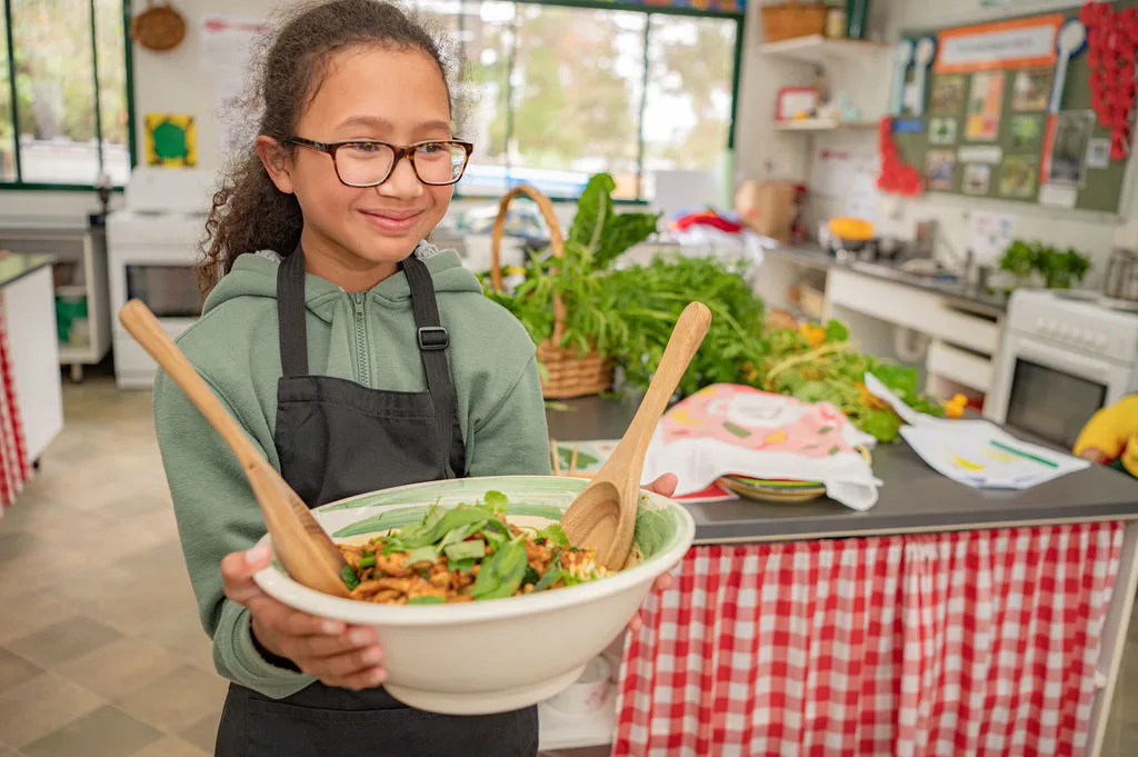 Stephanie Alexander Kitchen Garden Program child holding bowl of pasta with basil on top and two spoons sticking out of it