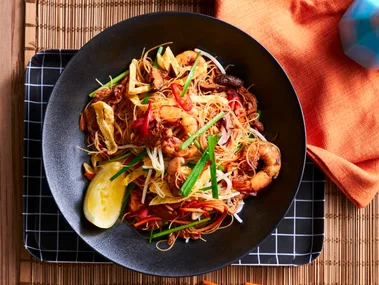 singapore noodles in black bowl with slice of lemon the side