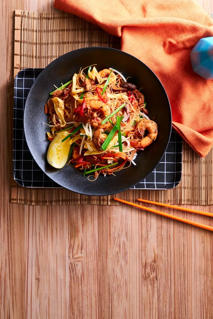 singapore noodles in black bowl with slice of lemon the side