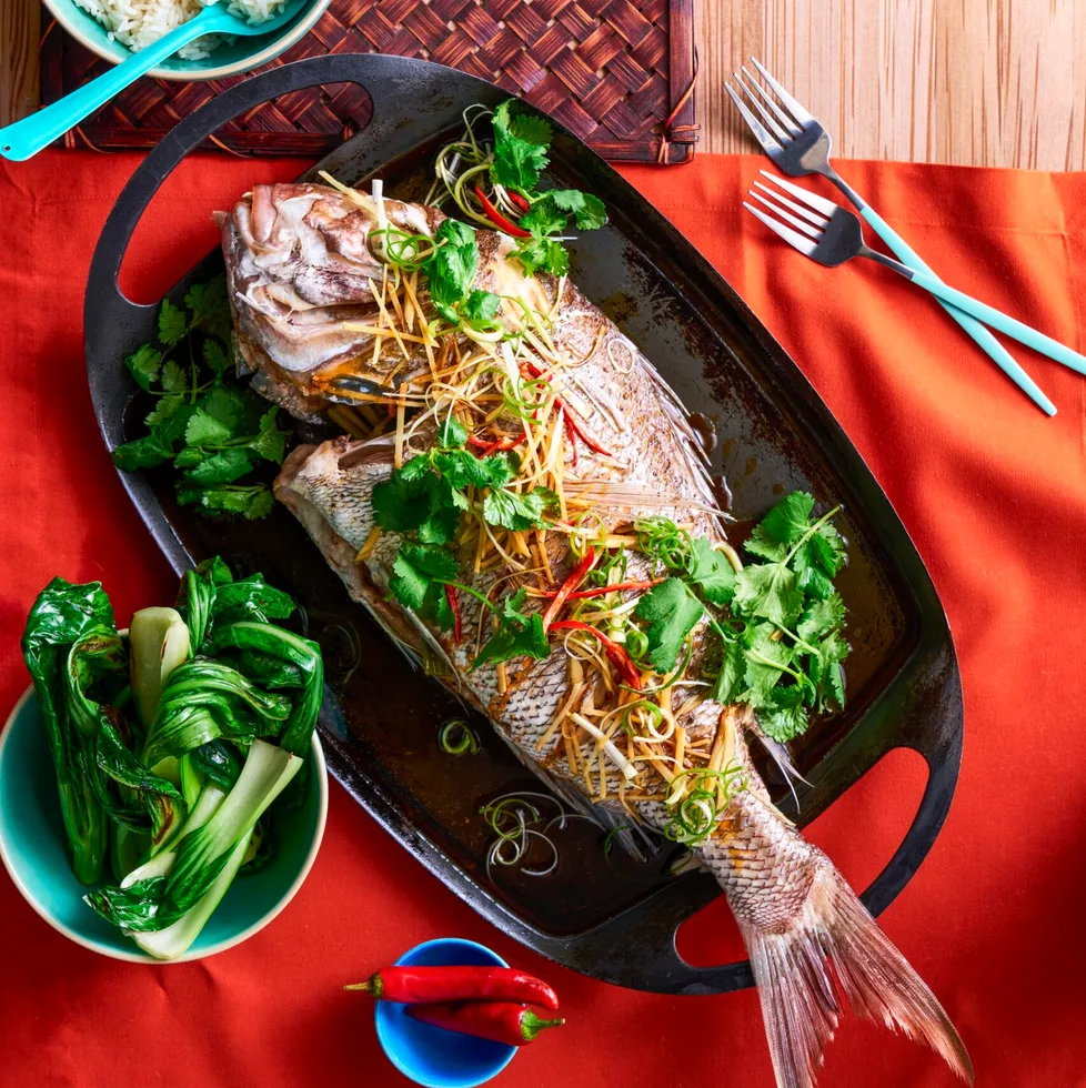 whole snapper fish with fresh herbs on top on black plate