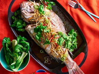 whole snapper fish with fresh herbs on top on black plate