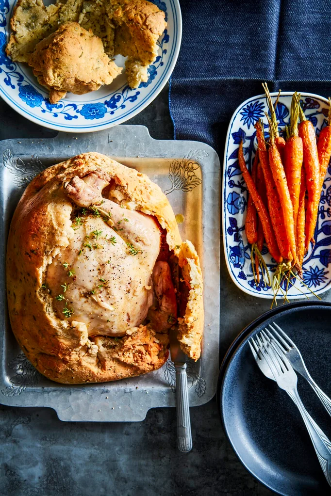 chicken in a salt crust with hole cut out of top with roasted carrots on the side