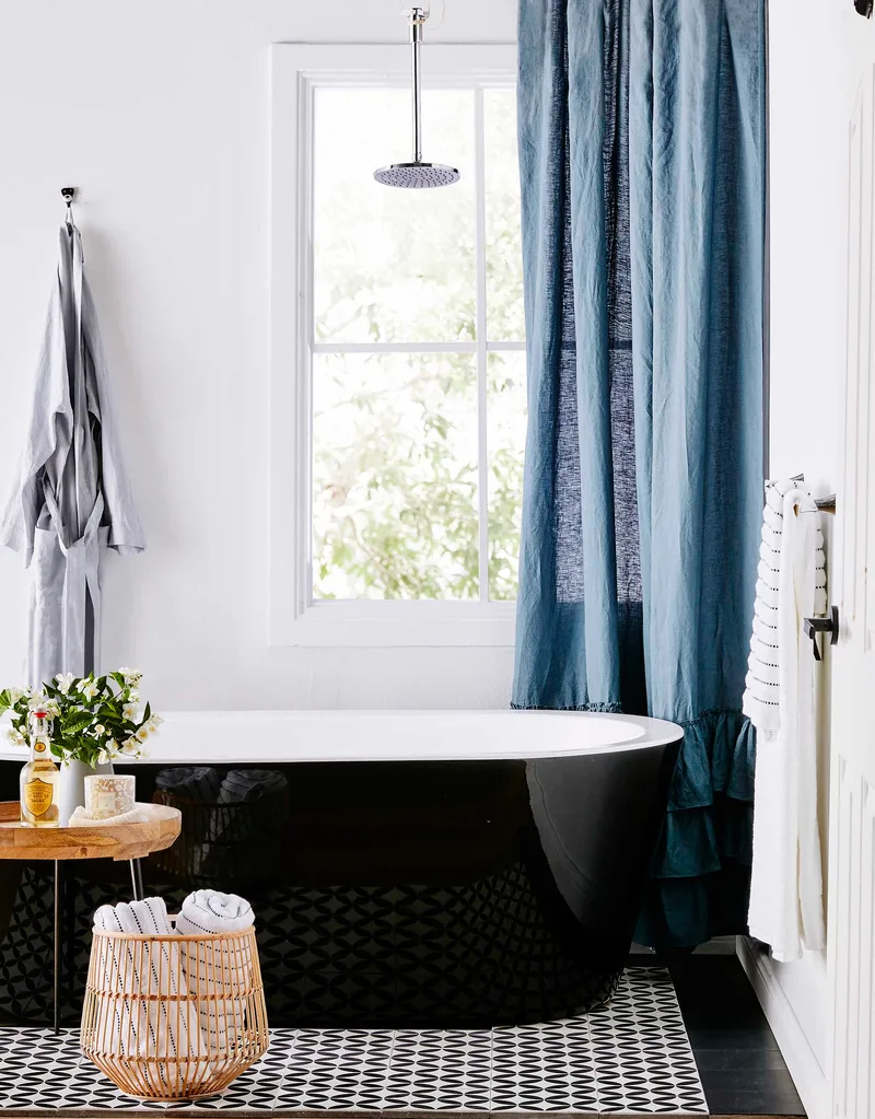 Black and white bathroom with gloss black bath tub and blue curtain