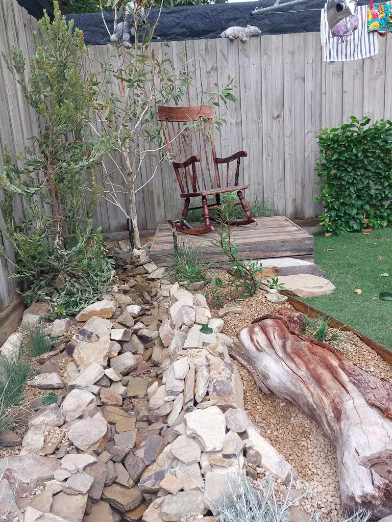 close up of creek bed in memories garden with rocks and driftwood to the side, and rocking chair on deck in the back