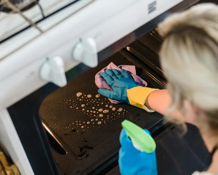 Person cleaning oven with spray and rubber gloves