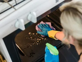 Person cleaning oven with spray and rubber gloves