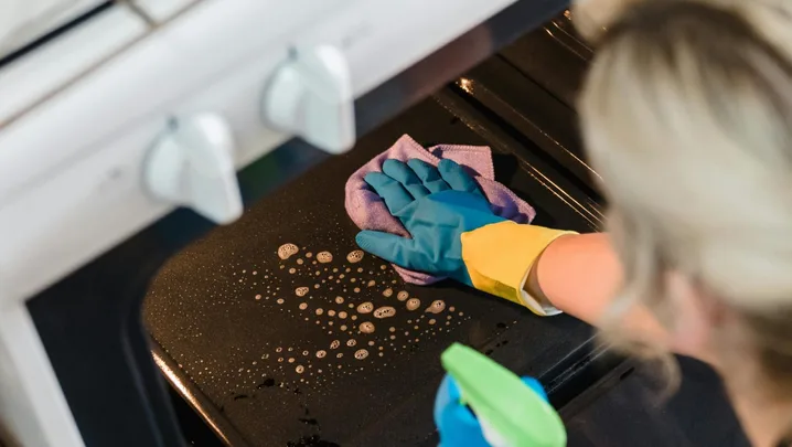 Person cleaning oven with spray and rubber gloves