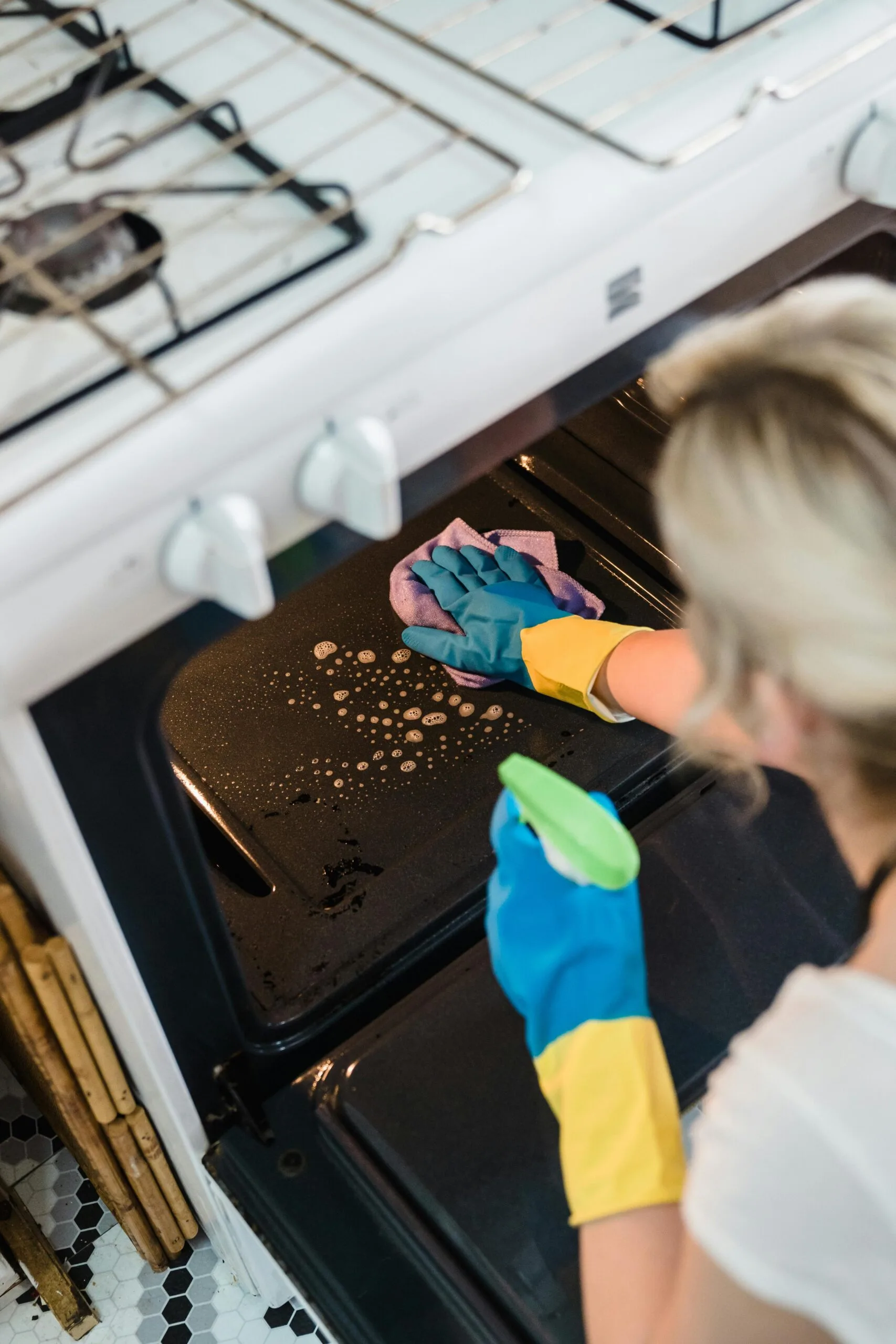 Person wearing rubber gloves cleaning the oven with soap, spray and microfibre cloth