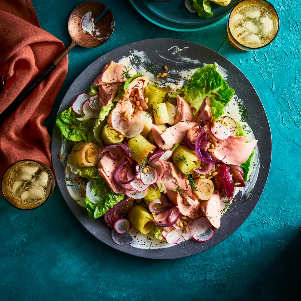 braised leeks poached trout salad in a black bowl on teal tablecloth