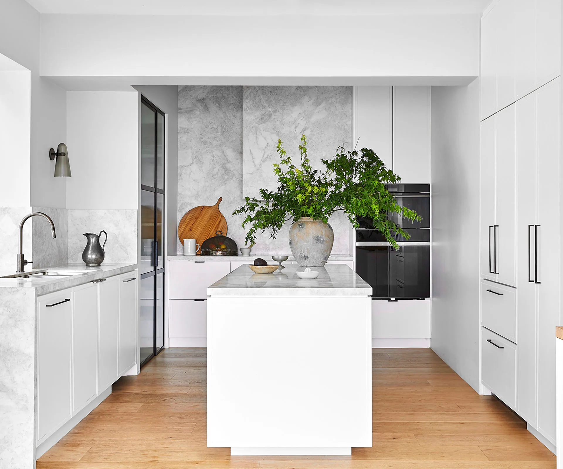 White kitchen with grey stone benchtop and splashback and timber flooring.