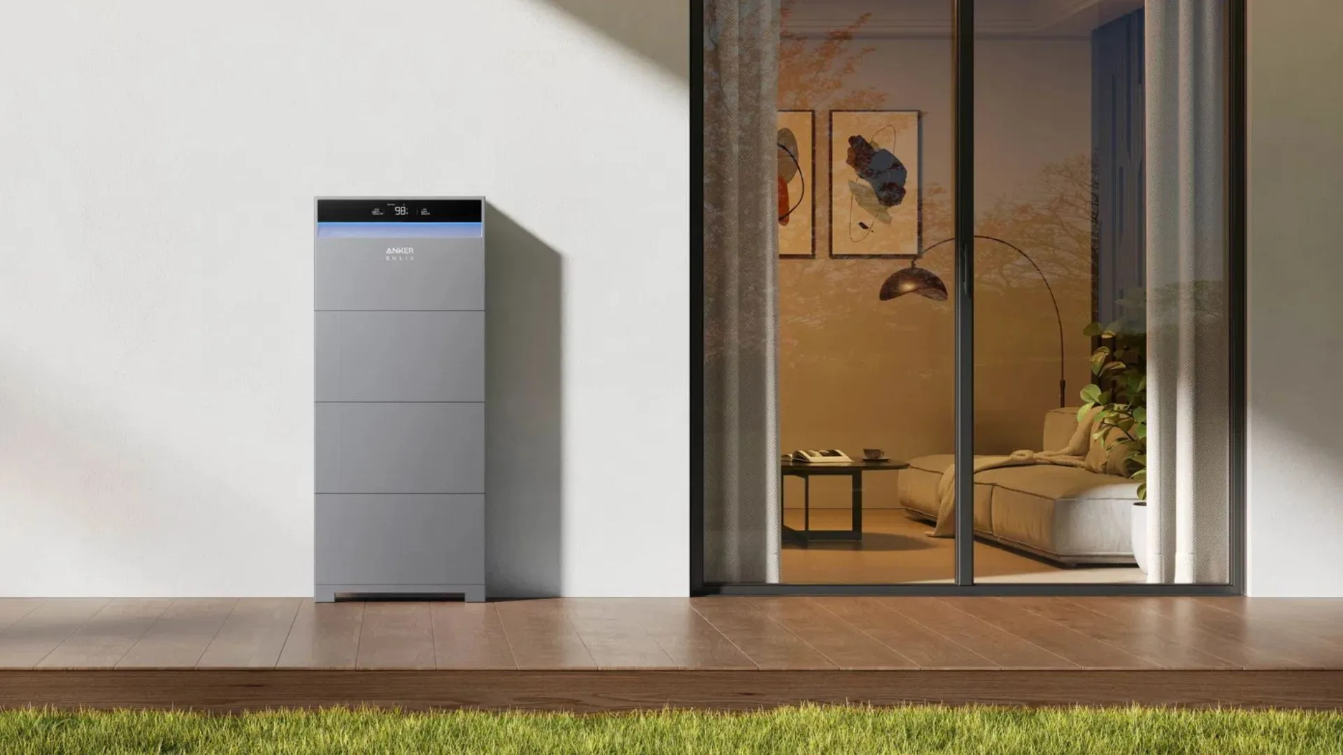 A tall, sleek Anker SOLIX home battery storage system sits on a wooden patio next to a glass sliding door, offering a glimpse into a modern living room.