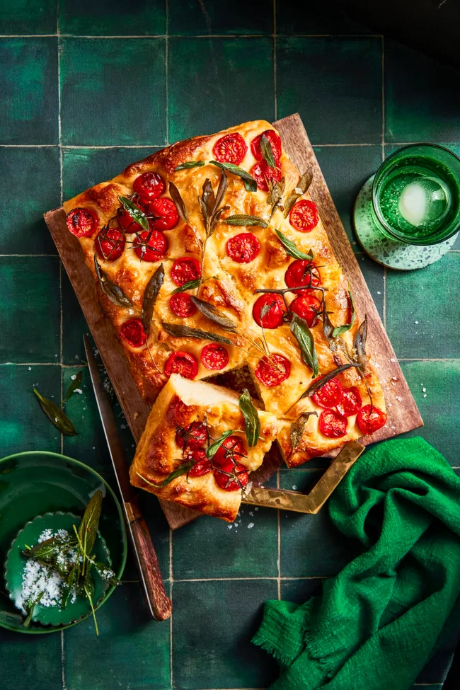 foccacia with piece balancing on top and cherry tomatoes in bread