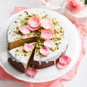 cake with white drip icing and crystallised rose petals on top and pistachio crumb