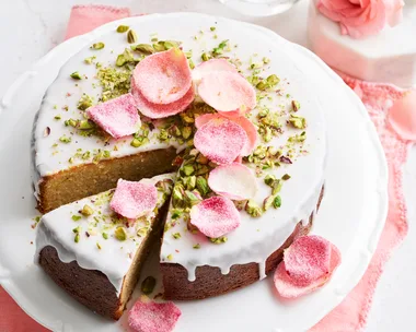 cake with white drip icing and crystallised rose petals on top and pistachio crumb