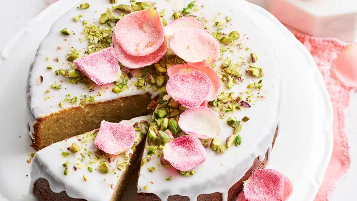 cake with white drip icing and crystallised rose petals on top and pistachio crumb